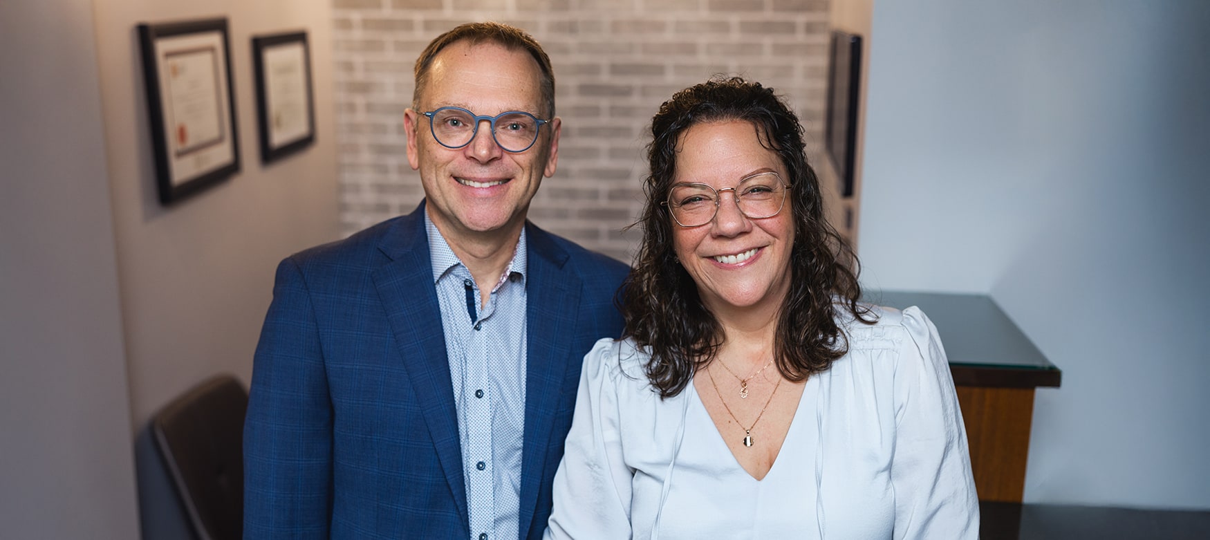 Dre Caty Goulet et Dr Steve Sénéchal souriants à la clinique chiropratique de Rivière-du-Loup, debout devant un mur de diplômes
